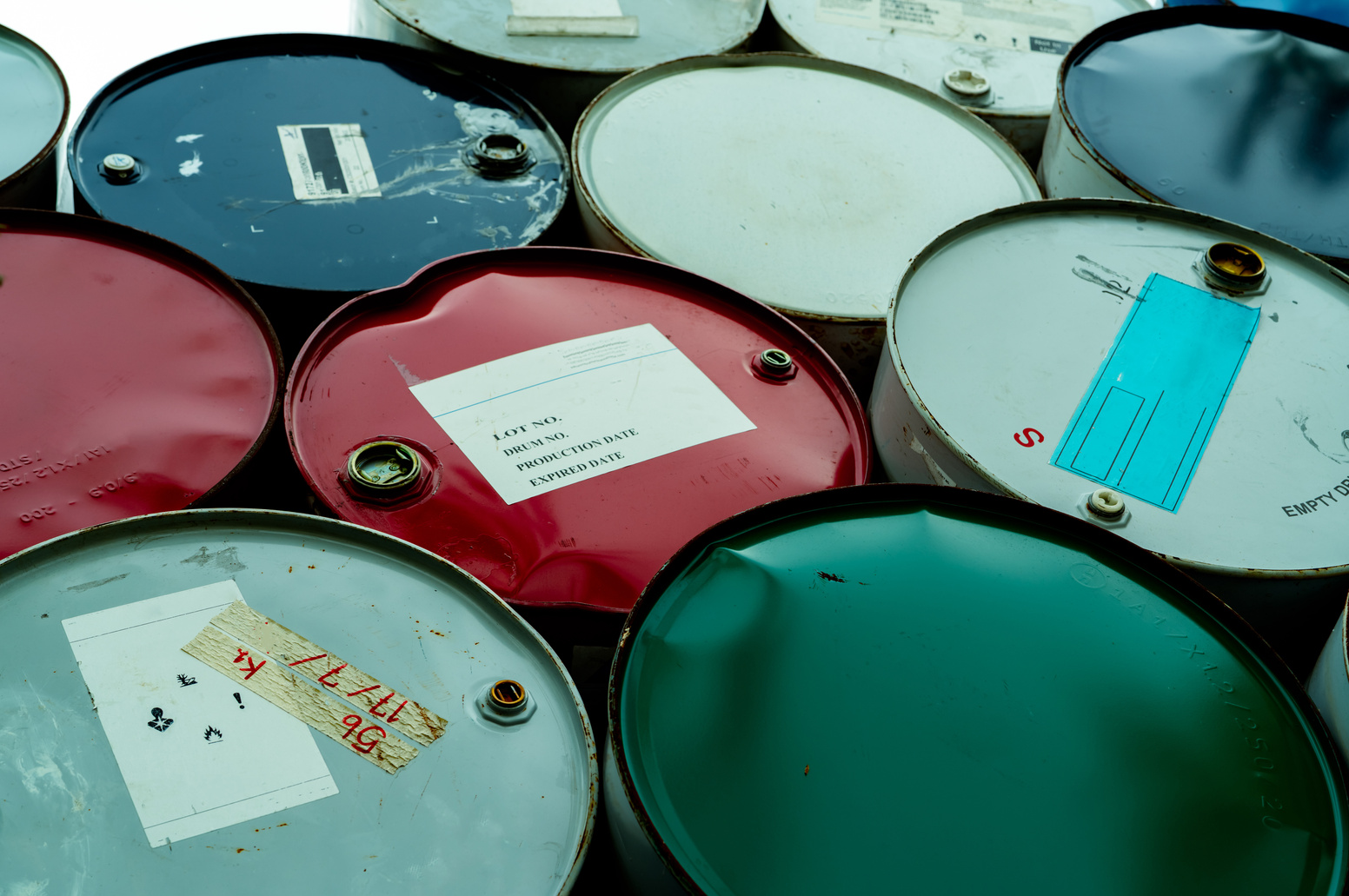 Old chemical barrels. Blue, green, and red oil drum. Steel oil tank. Toxic waste warehouse. Hazard chemical barrel with warning label. Industrial waste in drum. Hazard waste storage in factory.